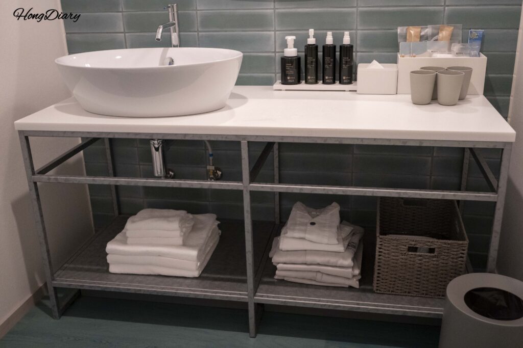 Bathroom dry zone at RISONARE Shimonoseki with vanity sink, fresh towels, folded pajamas, and osaji brand amenities
