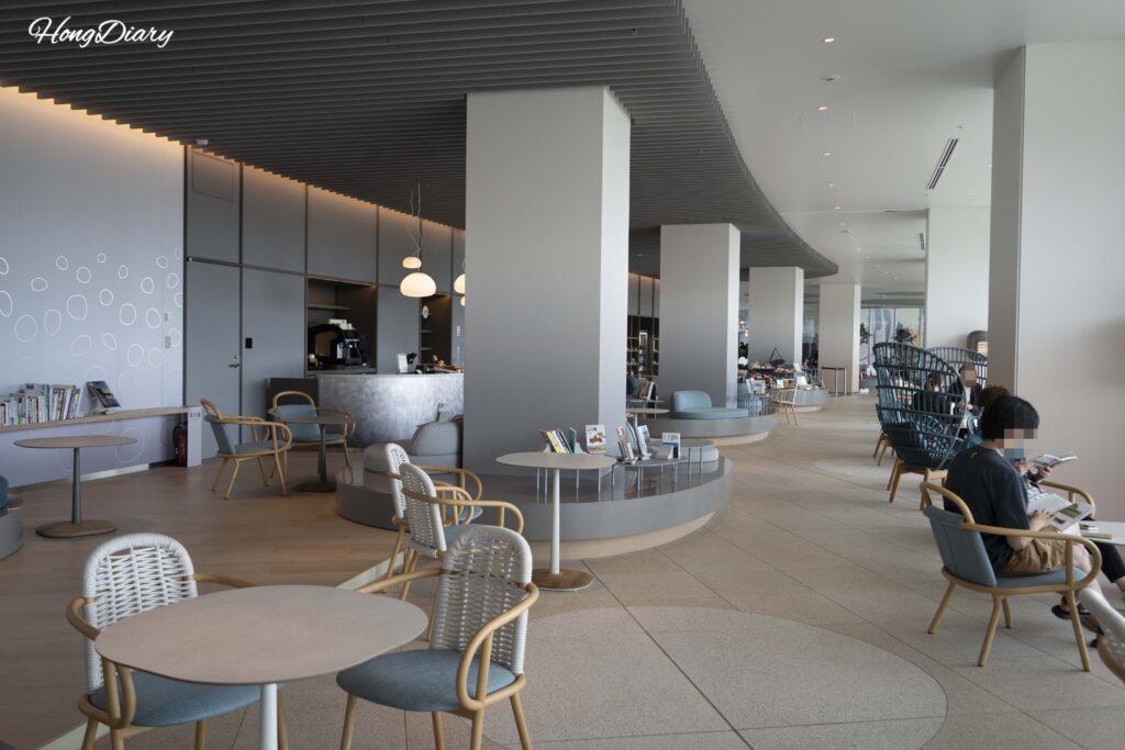 Book and Cafe lounge area at RISONARE Shimonoseki with guests relaxing on sofas surrounded by bookshelves