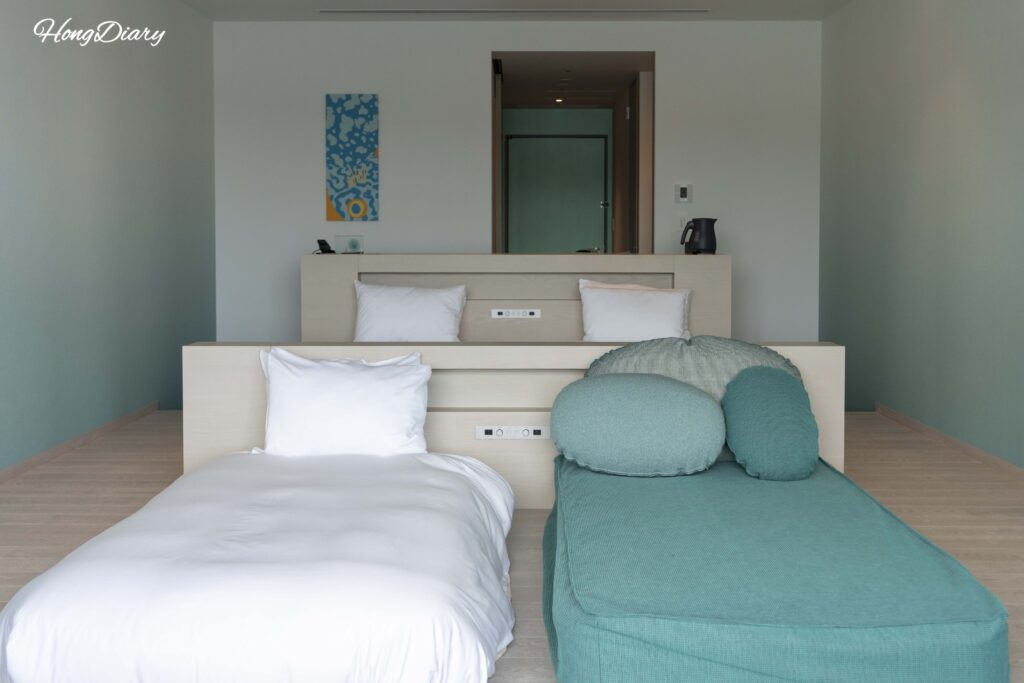 Deluxe Quad room interior at RISONARE Shimonoseki showing beds, desk, and sofa bed viewed from the window side