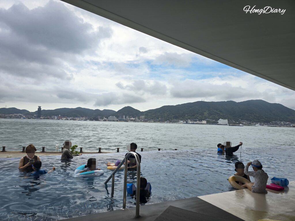 Piscina infinita de RISONARE Shimonoseki con bañistas y el Estrecho de Kanmon al fondo, agua a 38 °C