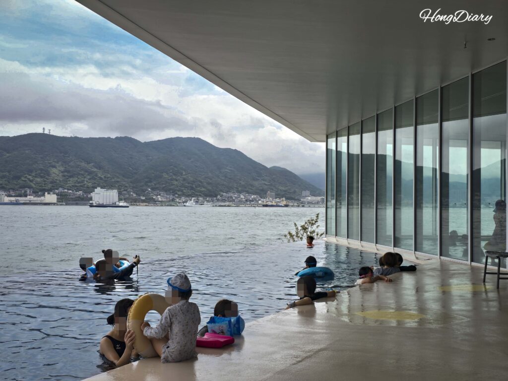 Outdoor infinity pool at RISONARE Shimonoseki with guests swimming and the Kanmon Strait stretching out beyond the pool edge