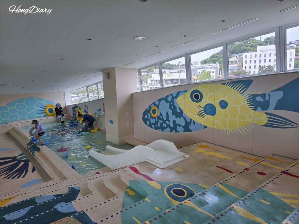 Children's wading pool and water slide area at RISONARE Shimonoseki Fugu Pool, with pufferfish illustrations on the walls