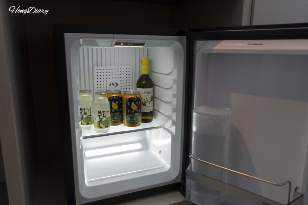 In-room mini-fridge at RISONARE Shimonoseki with a complimentary water bottle and selection of paid beverages