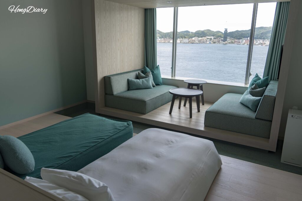 Beds and sofa bed in a Deluxe Quad room at RISONARE Shimonoseki with floor-to-ceiling windows overlooking the Kanmon Strait