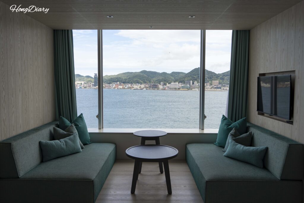 Window-side sofa and table in a Deluxe Quad room at RISONARE Shimonoseki with Mojiko and Kyushu visible across the Kanmon Strait