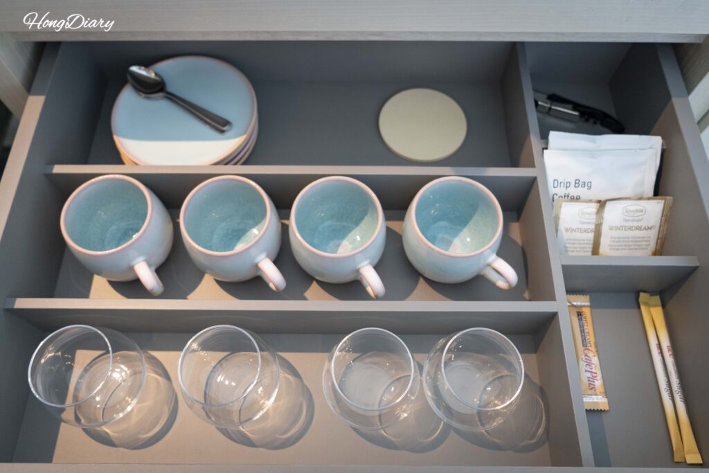 In-room tea and coffee set at RISONARE Shimonoseki including water glasses, cups, tea bags, and drip coffee packets stored in a desk drawer