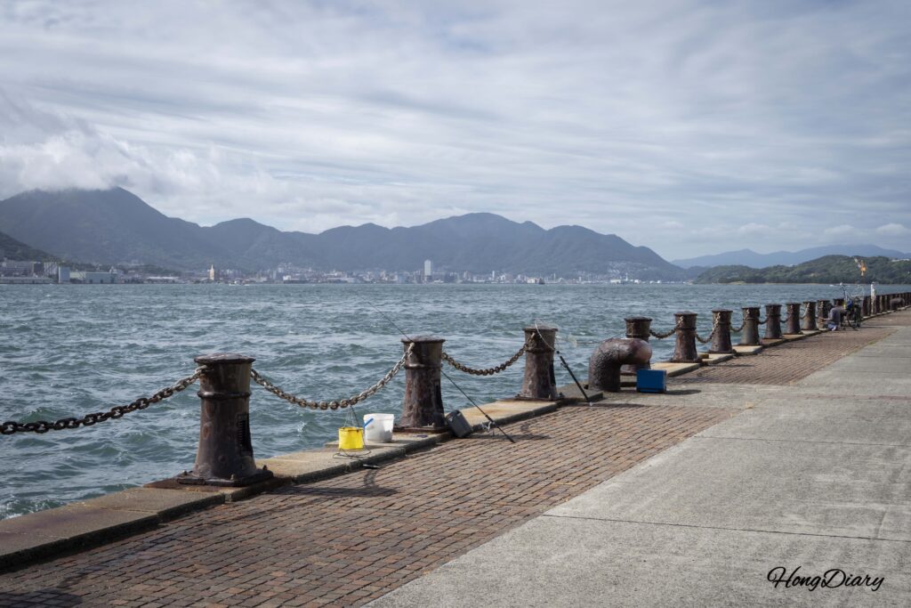 Mar agitado frente a RISONARE Shimonoseki con un pescador local en la orilla