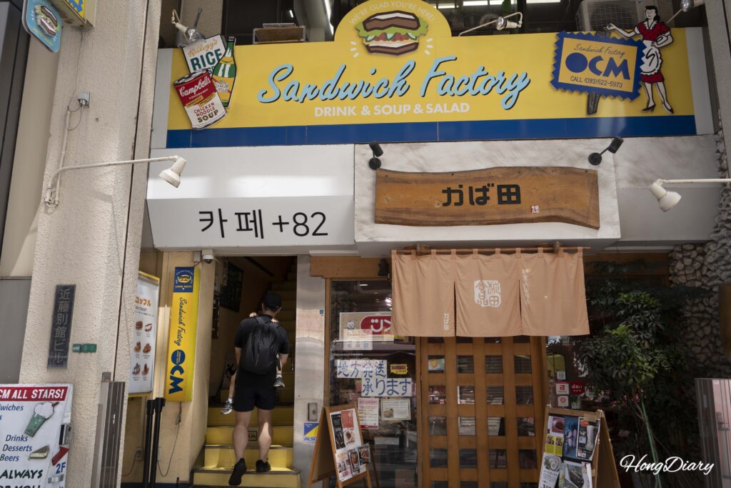 Exterior of the building housing Sandwich Factory OCM in Kokura, Kitakyushu, with a family heading up the yellow staircase to the second floor