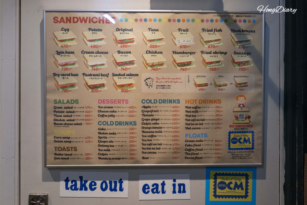 Carta completa de Sandwich Factory OCM en Kitakyushu con todos los rellenos de sándwich, acompañamientos, bebidas y precios en inglés y japonés, con aviso de comer adentro y para llevar