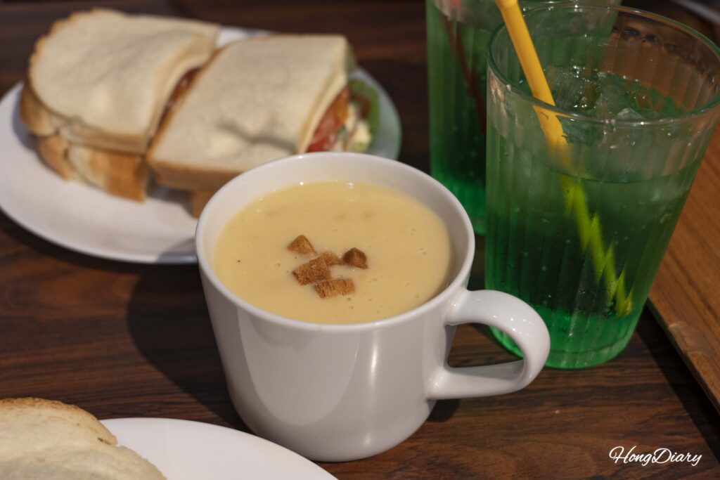 Japanese-style corn soup at Sandwich Factory OCM with a sandwich and melon soda visible in the background