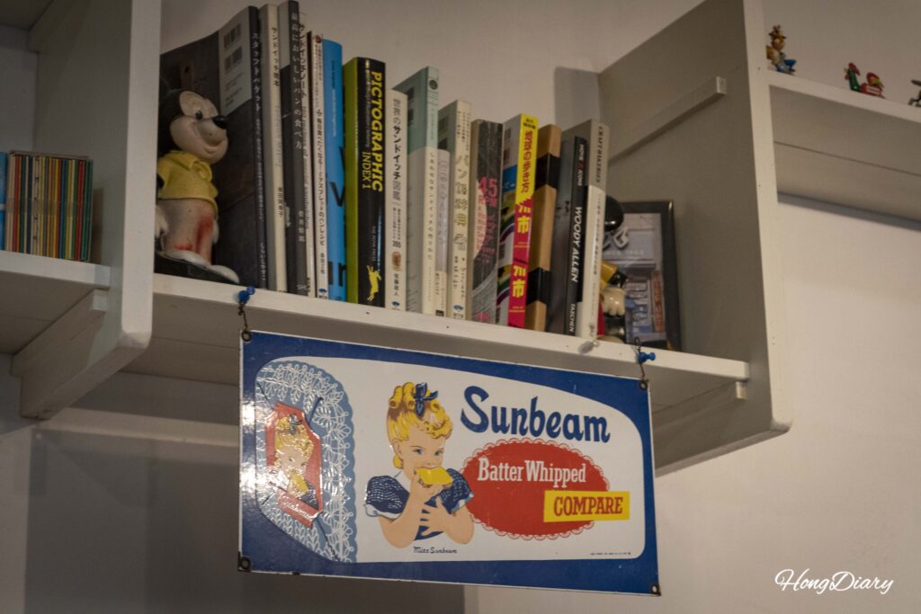 Póster metálico retro de Sunbeam y libros japoneses como parte de la decoración interior de Sandwich Factory OCM en Kitakyushu