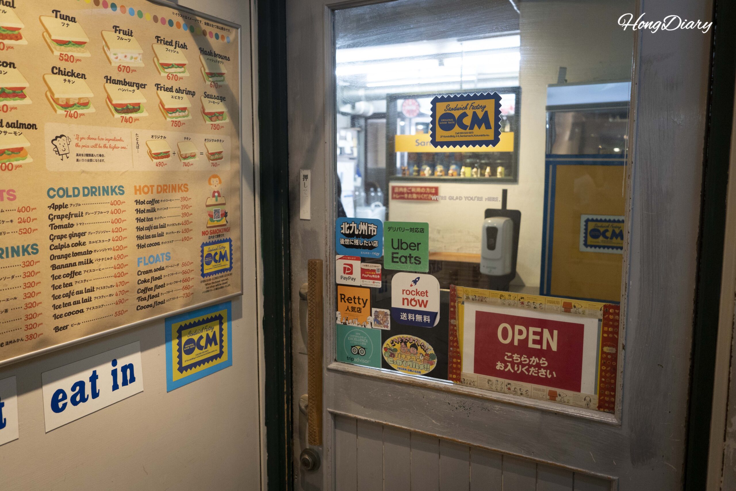 Entrada del segundo piso de Sandwich Factory OCM con una carta bilingüe en inglés y japonés junto a la puerta