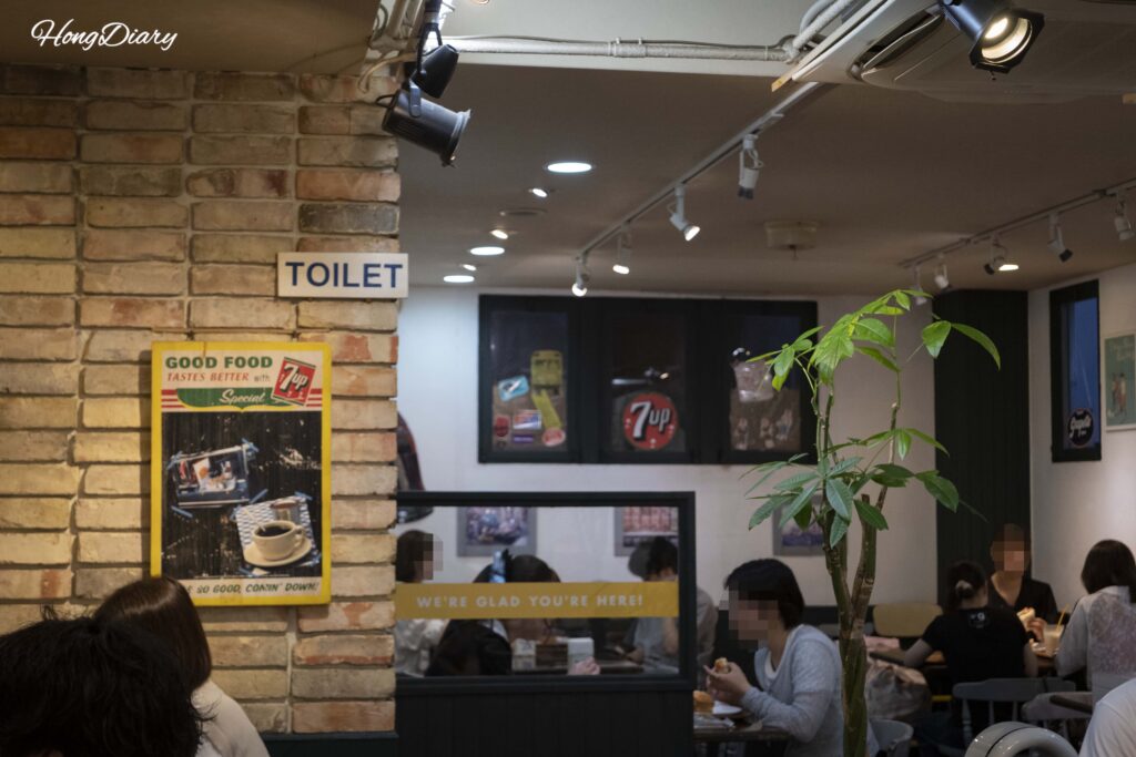 Interior del comedor de Sandwich Factory OCM en Kitakyushu con clientes disfrutando sándwiches en mesas para dos y cuatro personas