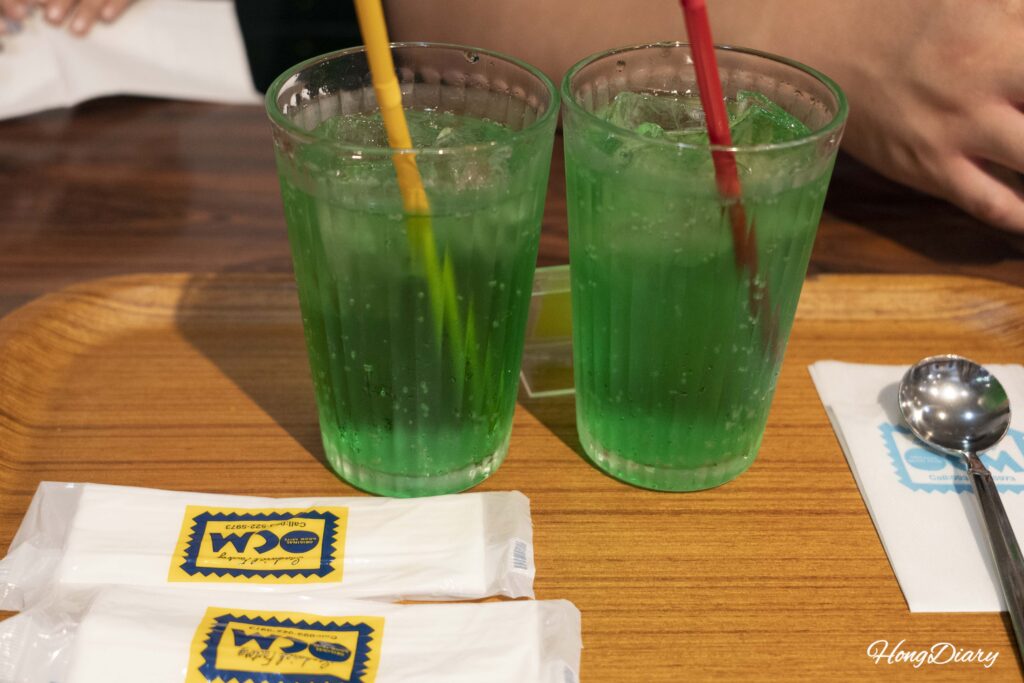 Bright green Japanese melon soda at Sandwich Factory OCM with a wet towel napkin underneath the glass