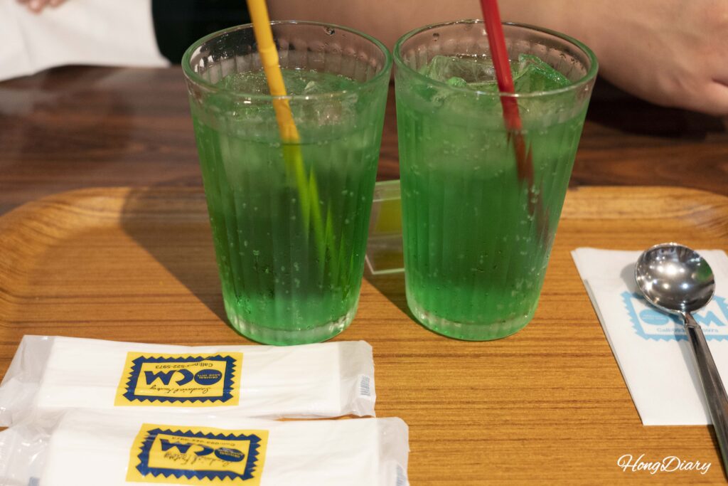 Refresco japonés melon soda de color verde intenso en Sandwich Factory OCM con una toallita húmeda debajo del vaso