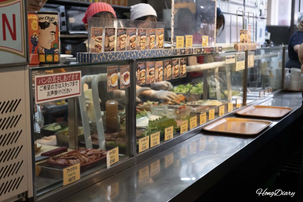 Mostrador de pedidos de OCM en Kokura con fotos de combinaciones recomendadas en inglés y japonés e ingredientes frescos visibles detrás del vidrio