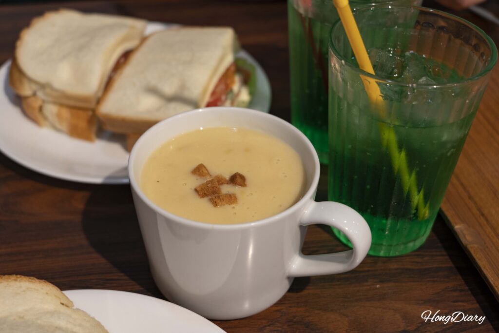 Sopa de maíz al estilo japonés en Sandwich Factory OCM con un sándwich y melon soda visibles al fondo